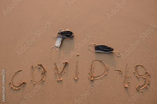 Pandemia of coronavirus. Sign on the sand covid-19 and used medical mascs lie next to. Ocean polution photo