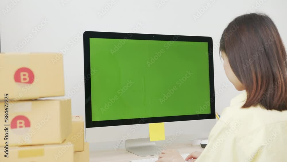 Startup small business, Young Asian woman checking online order on computer with green screen. and packing boxes for products to send to customers. Startup small business, Young Asian woman checking online order on computer with green screen. and packing boxes for products to send to customers.