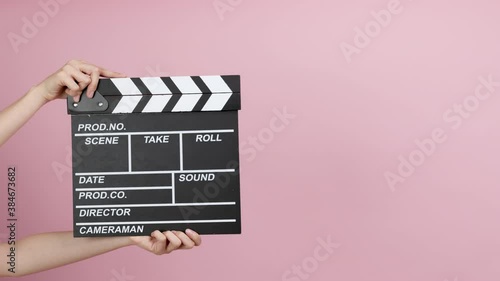Close up female hold making movie production clapperboard on pink background.