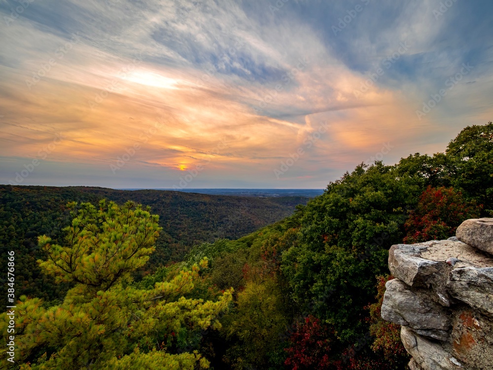 Sunset over the mountains of West Virginia from Coopers Rock Overlook in Coopers Rock State Forest.  A blue and orange sunset sky over fall foliage trees in red, green and yellow.