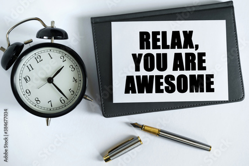 On the table there is a clock, a pen, a notebook and a card on which the text is written - RELAX, YOU ARE AWESOME