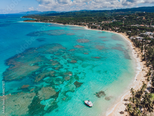 Aerial drone panoramic view of the paradise beach with sandy shore, coral spots, palm trees, color boats and blue water of Atlantic Ocean, Las Terrenas, Samana, Dominican Republic