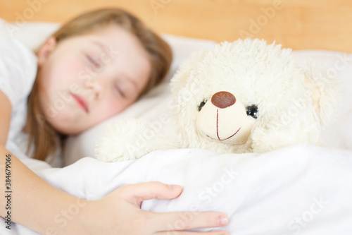 girl is sleeping with a soft toy on white bed
