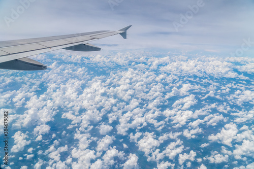 Aerial view above clouds from airplane window with blue sky. Tropical climate in Thailand.