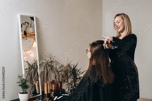 A female hairdresser of European appearance works with the hair of a model. Home beauty salon. Barbershop. Healthy strong hair.