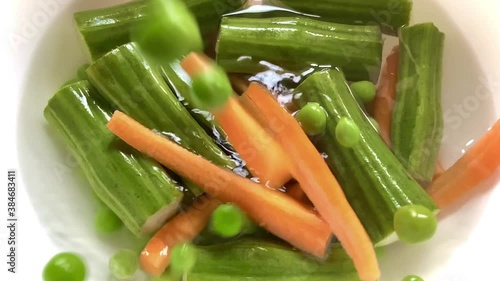 Dropping fresh green organic peas carrots into a dish of drumstick pieces filled with water