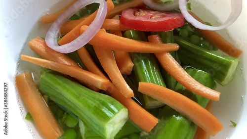 In a bowl of water with carrots fresh organic green peas tomato slices and cut moringa random veggies like onion rings tomatoes and raw plantain being dropped 