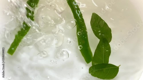 Pouring water into a bowl with leaves and green chilies as eggplant or aubergine and onions are dropped creating beautiful splashes bubbles and ripples