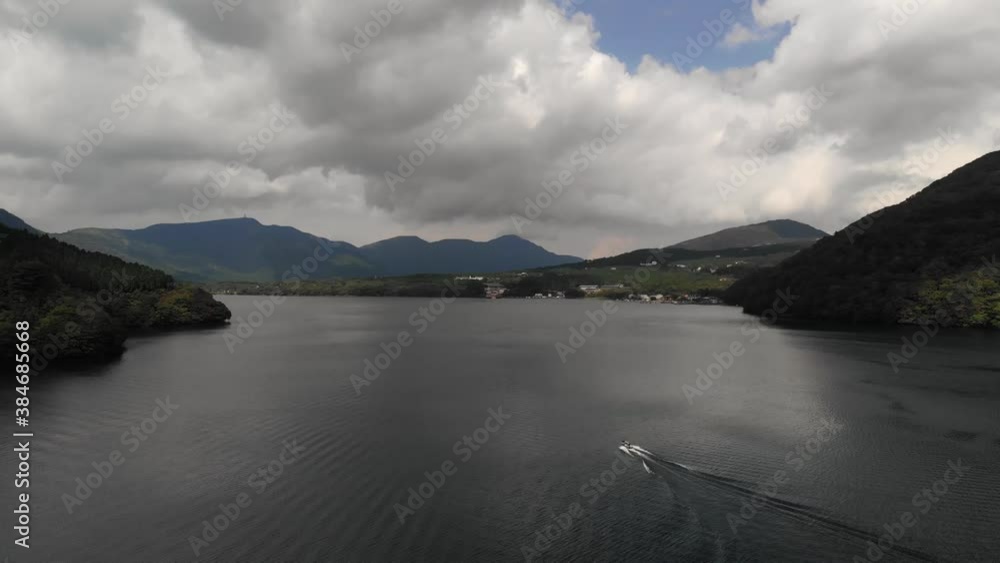 Tracking aerial drone shot of speedboat on lake with mountains in distance on clear day Tracking aerial drone shot of speedboat on lake with mountains in distance on clear day