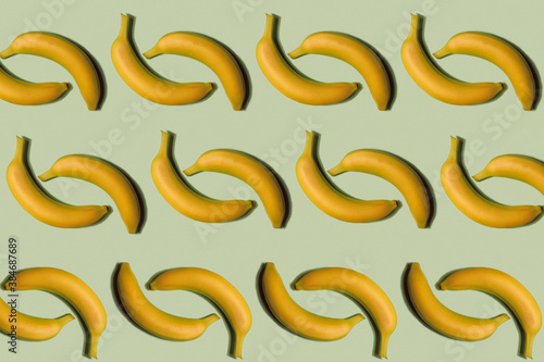 Fruit pattern. Repeating whole bananas on a light green background. Interesting fruit pattern made from natural fruits. Horizontal. The concept of healthy food and vegetarianism.