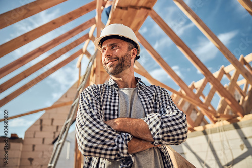 Pleased man in a hard hat posing under a wooden roof