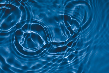 De-focused transparent dark blue colored clear calm water surface texture with splashes and bubbles. Trendy abstract nature background. Water waves in sunlight with copy space.
