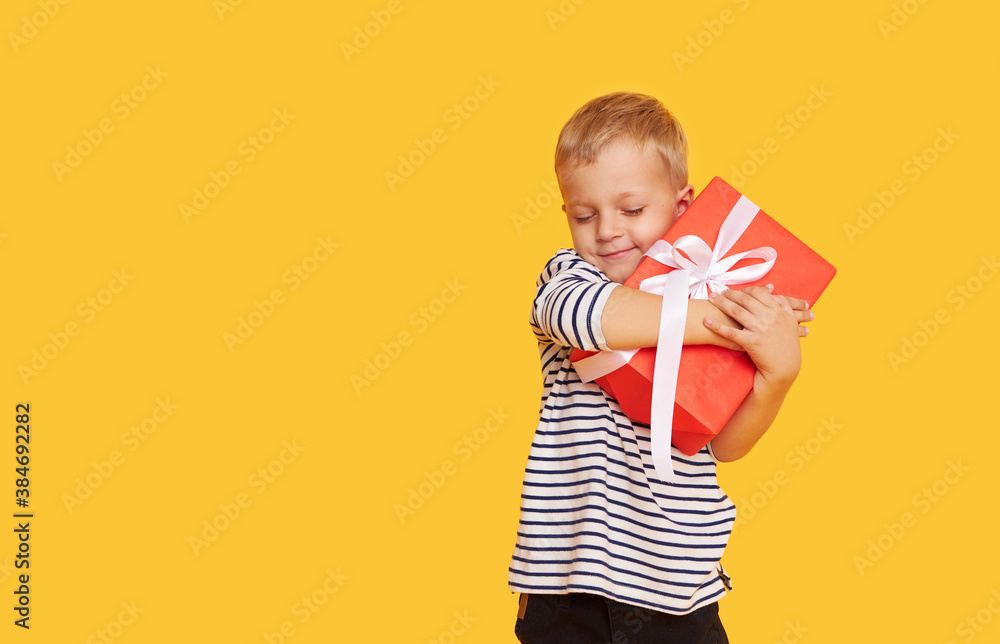 Fototapeta premium Studio shot of happy child boy celebrating holiday, unpacking gift box with excited face, posing over yellow background