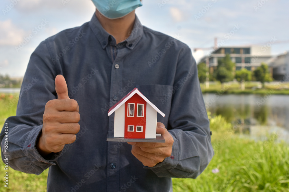 Man wear medical mask holding house model concept business finance sale rent real estate Man wear medical mask holding house model concept business finance sale rent real estate