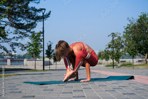 Young attractive woman in red sportswear practices yoga exercises outdoors.