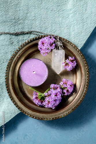 Verbena flowers, candle, and a crystal vial for essential oils, overhead shot on a blue background