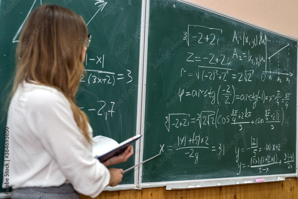 Young college student writing mathematical exercise on the chalkboard during a class Young college student writing mathematical exercise on the chalkboard during a class