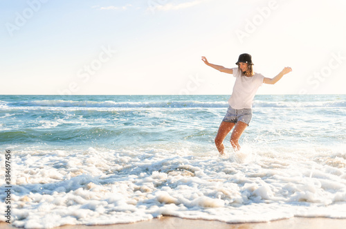 Funny young woman playful on sunset beach. Beautiful happy female on the shore of the blue sea having fun playing splashing water, positive mood, summer vacation, sunny concept