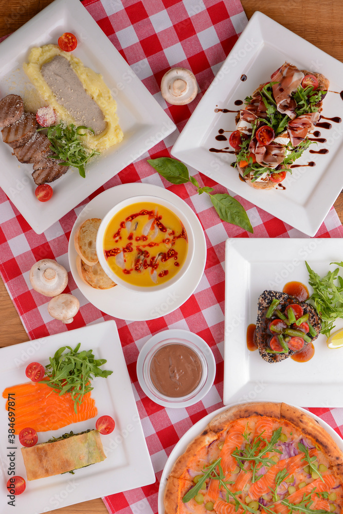 Flat lay shot of delicious italian cuisine. Delicious pizza, salmon rolls, pumpkin soup and salad on a wooden table. Flat lay shot of delicious italian cuisine. Delicious pizza, salmon rolls, pumpkin soup and salad on a wooden table.