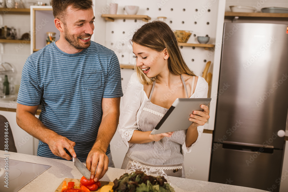 Young couple cooking together in kitchen reading recipes on digital tablet.