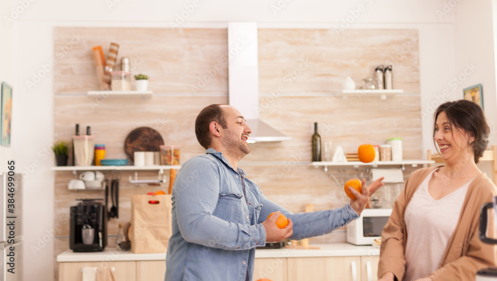 Man juggle with oranges for woman while preparing tasty and nutritious smoothie. Healthy carefree and cheerful lifestyle, eating diet and preparing breakfast in cozy sunny morning Man juggle with oranges for woman while preparing tasty and nutritious smoothie. Healthy carefree and cheerful lifestyle, eating diet and preparing breakfast in cozy sunny morning