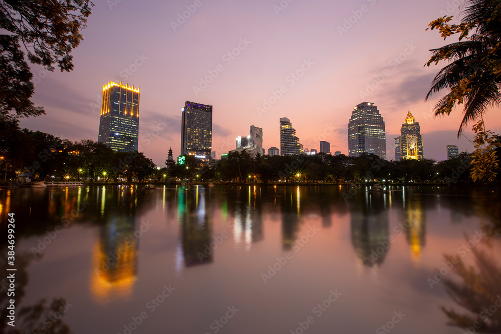 Cityscape of the tail building with reflaction of water in the sunset at Lumpini park , Bangkok , Thailand.