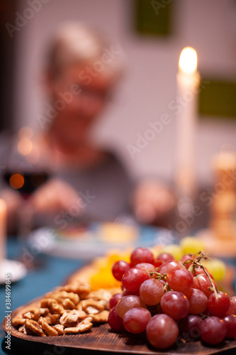 Nuts and grapes sitting on wooden plate during elderly couple festive dinner. Senior couple sitting at the table in kitchen, talking, enjoying the meal, celebrating their anniversary in the dining
