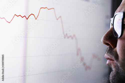 A businessman is looking at a graph on a monitor. An exchange broker evaluates stock market trends. A man with glasses in front of a curve of the dynamics of the economy.