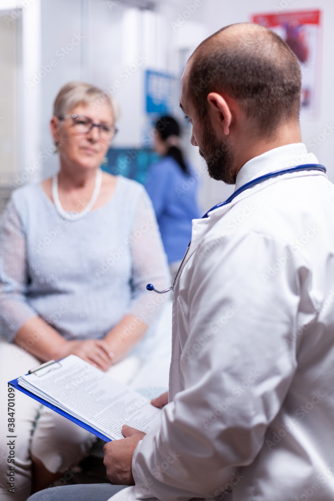 Obraz premium Doctor holding medical document while speaking with senior old woman in clinic cabinet. Converstation with medical stuff clinic medicine healthcare, senior, coat, clipboard.
