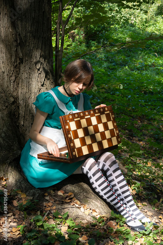 Alice in wonderland. A girl with a chessboard sits under a huge tree.