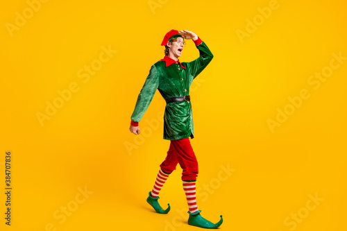 Full length body size view of his he nice attractive glad amazed cheerful cheery funny guy elf walking looking meet winter party isolated over bright vivid shine vibrant yellow color background