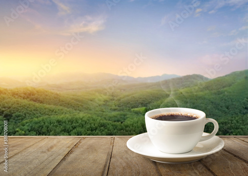 White cup of hot coffee on wooden table with the mountain background.