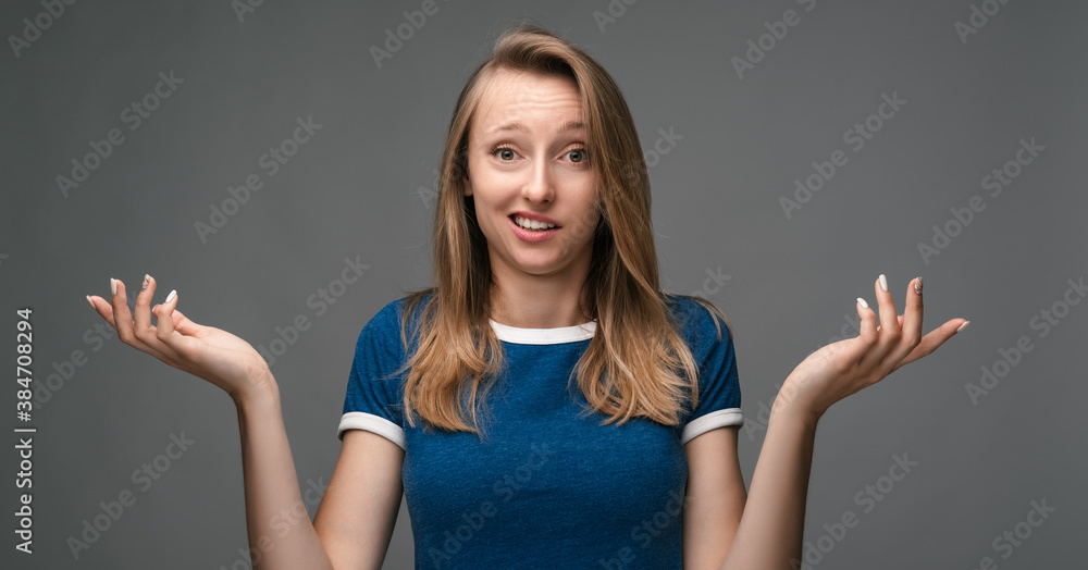 Pretty girl shrugging shoulders over gray background. Concept of doubt, uncertainty and confusion Pretty girl shrugging shoulders over gray background. Concept of doubt, uncertainty and confusion