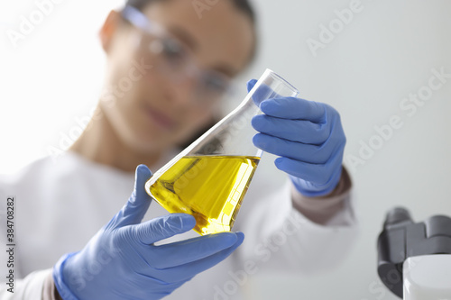 Female hands in rubber gloves holding flask with urine analysis in clinical laboratory closeup. Research on quality of oil products concept.