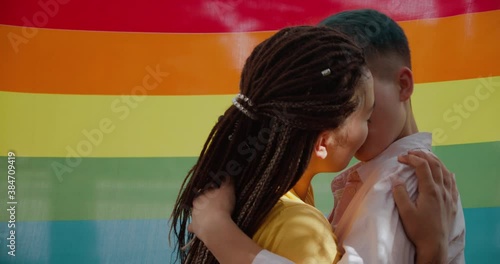 Young lesbian couple passionately kissing, lgbt rainbow flag background, love