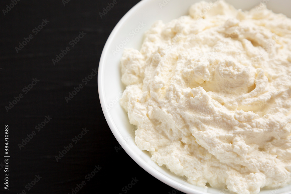 Tasty Ricotta Cheese in a white bowl on a black background, low angle view. Copy space.
