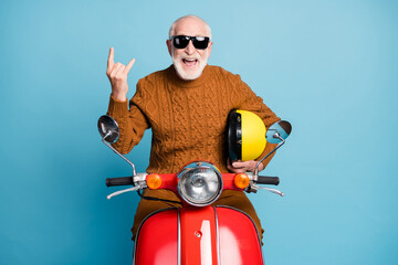 Portrait of his he nice attractive funky cheerful cheery cool naughty bearded grey-haired man hipster sitting on moped showing horn symbol isolated over blue pastel color background
