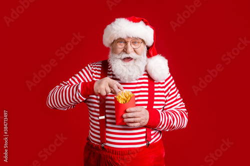 Portrait of his he nice handsome cheerful cheery hungry bearded Santa father eating fried delicious potato delivery lunch snack newyear isolated bright vivid shine vibrant red color background © deagreez