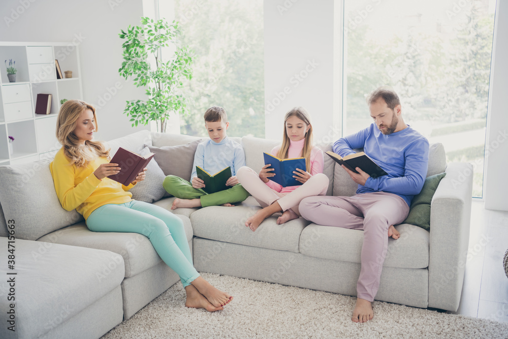 Full size photo of focused family mom dad two little kids boy girl sit couch read book in house indoors Full size photo of focused family mom dad two little kids boy girl sit couch read book in house indoors