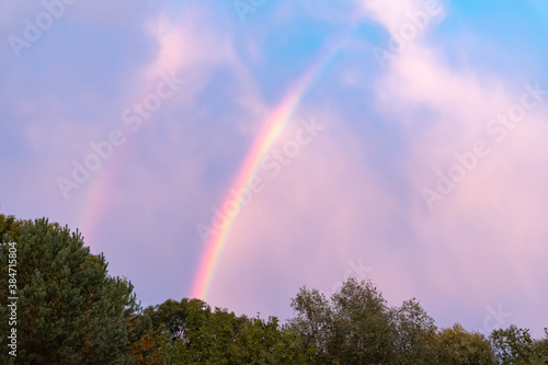 Double rainbow above forest with blue sky after the rain. Colorful clouds.