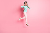 Full length body size photo of crazy little hispanic girl jumping up shouting wearing earphones isolated on pink color background