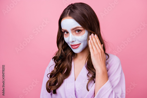Photo portrait of shy pretty tender girl applies skincare facial mask smiling touching brown wavy hair wearing bathrobe isolated on pink color background © deagreez