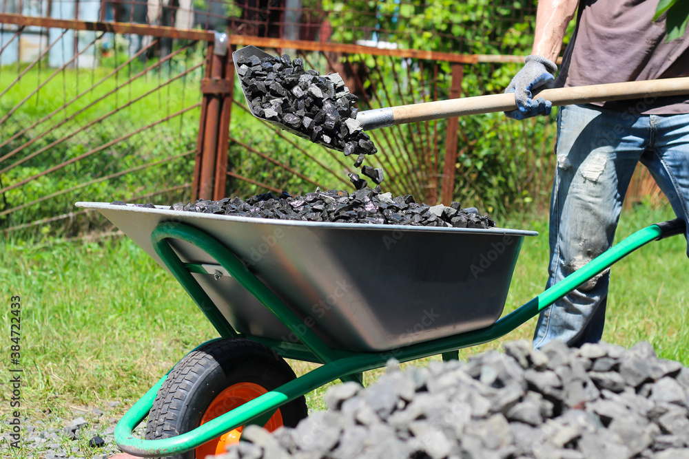 Man with the help of shovel loading crushed stones in the wheelbarrow. Laying the foundation