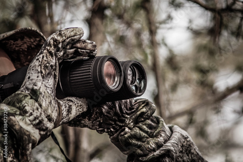 hunter in a camouflage suit looks through binoculars on the hunt, close-up, soft focus