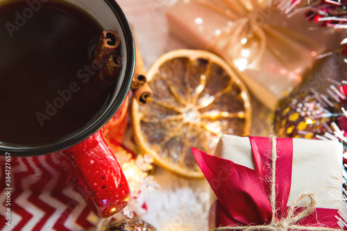 Red mug with tea and cinnamon sticks  a slice of dried orange  Christmas decor  gift boxes and garlands on the table. Flat lay. New Year