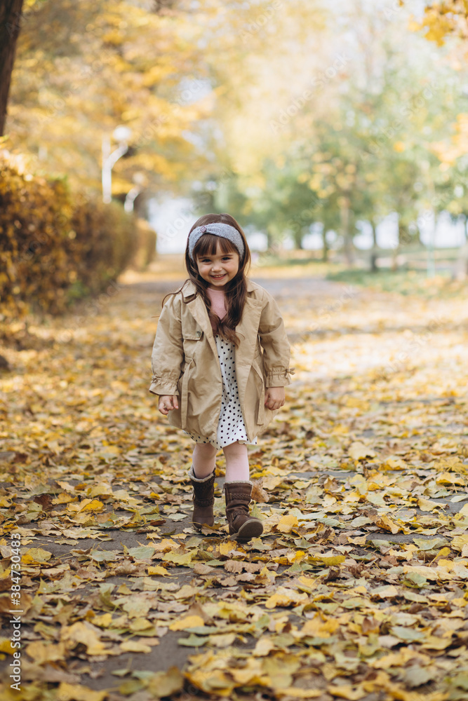 Happy and beautiful little girl in a beige coat walks in the autumn park Happy and beautiful little girl in a beige coat walks in the autumn park