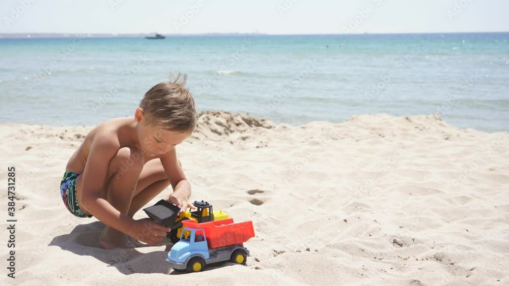 Blond boy is playing sitting on a sandy beach against the backdrop of a beautiful azure sea on a Sunny summer day. Blond boy is playing sitting on a sandy beach against the backdrop of a beautiful azure sea on a Sunny summer day.