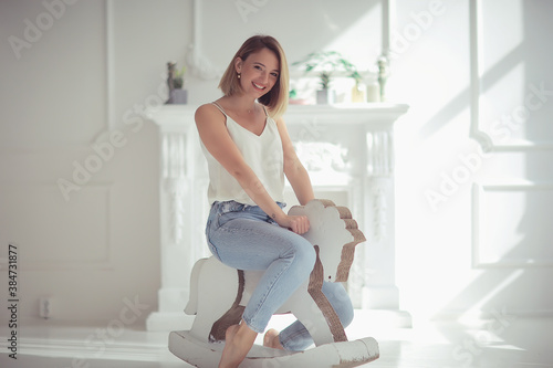 young adult girl on a rocking horse / unusual photo of a girl in the studio funny laugh