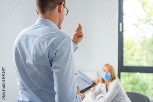 Work in a corporation during a pandemic. The man is giving a presentation and the woman wearing the face mask. Two business colleagues wearing protective face mask on a meeting during coronavirus.
