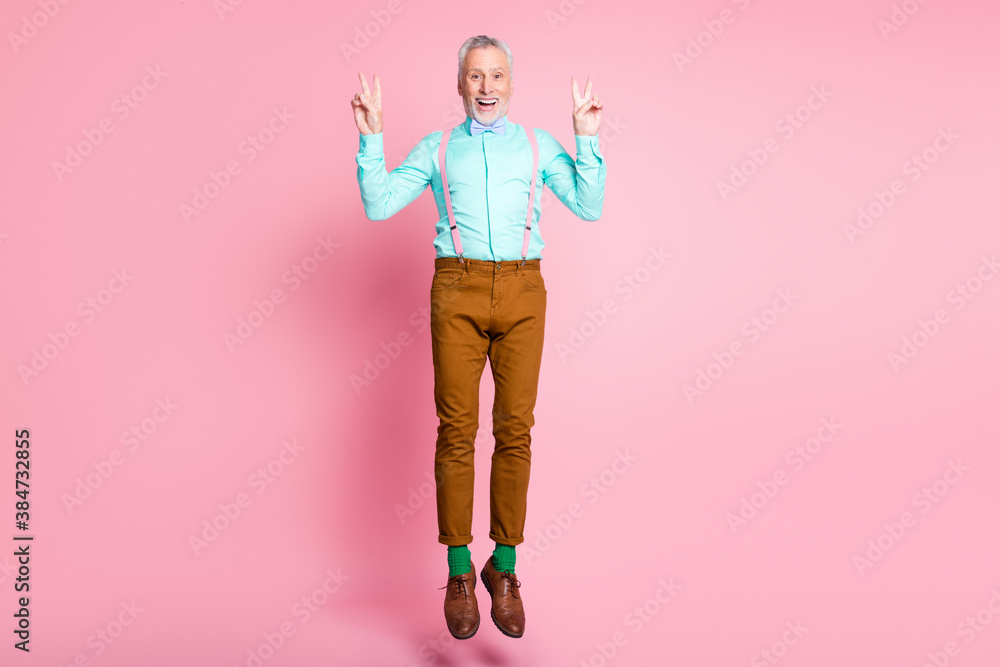 Full length body size side profile photo of happy old man jumping showing gesture v-sign with both hands isolated on pink color background Full length body size side profile photo of happy old man jumping showing gesture v-sign with both hands isolated on pink color background
